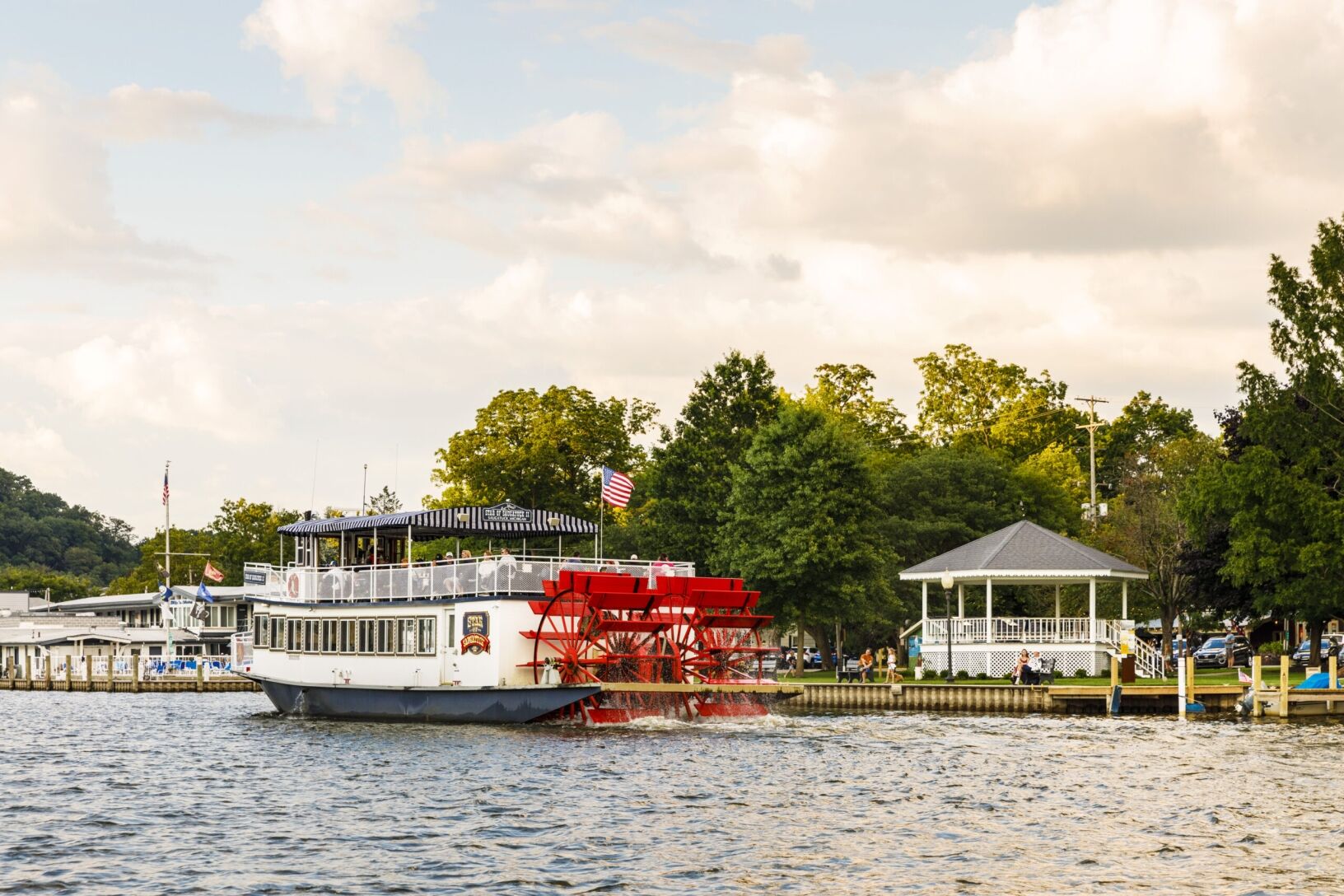 The Star of Saugatuck sailing in the water as people in Wicks Park relax.