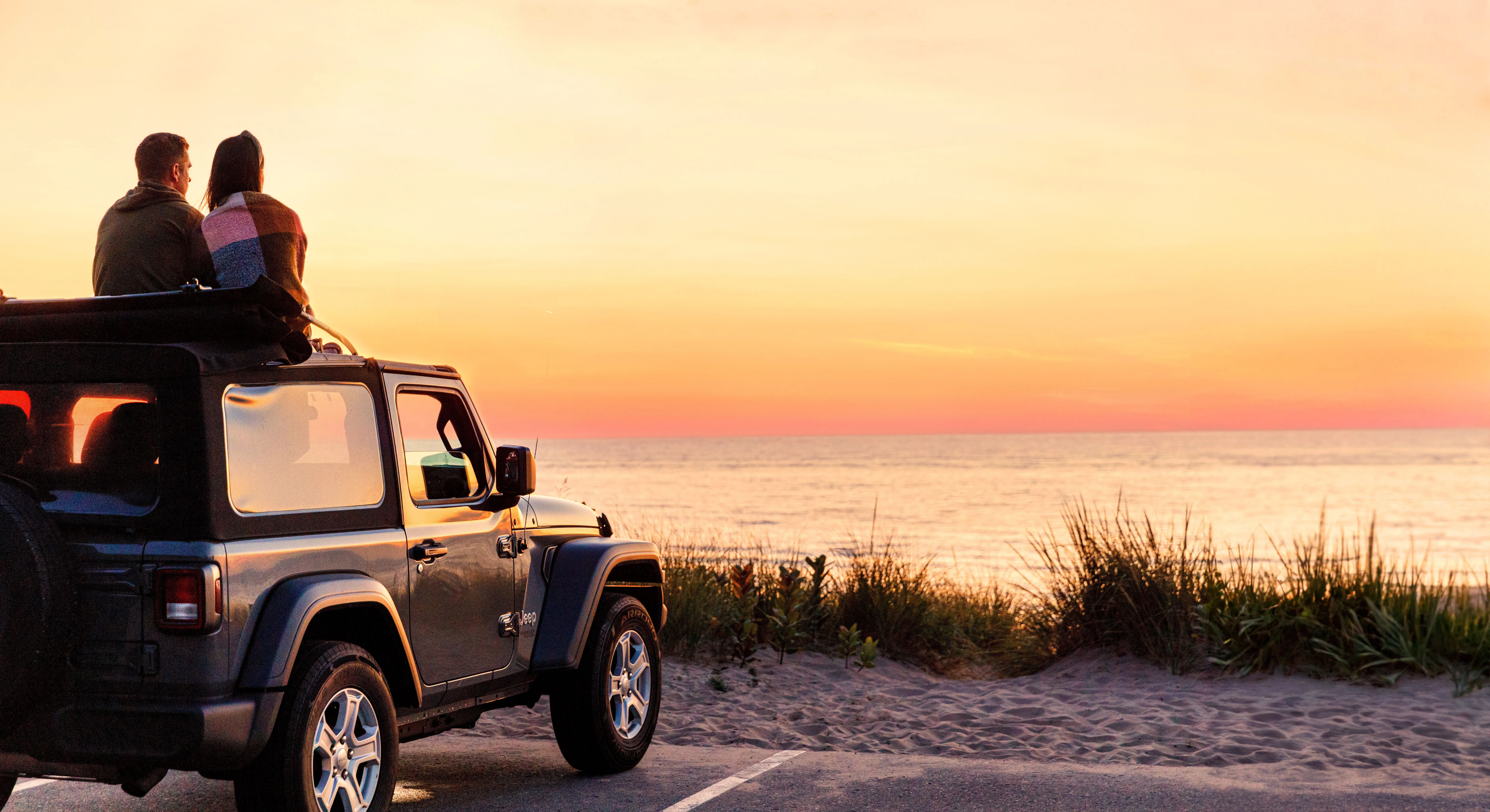 A couple watching the sunset from the top of their Jeep at Oval Beach.