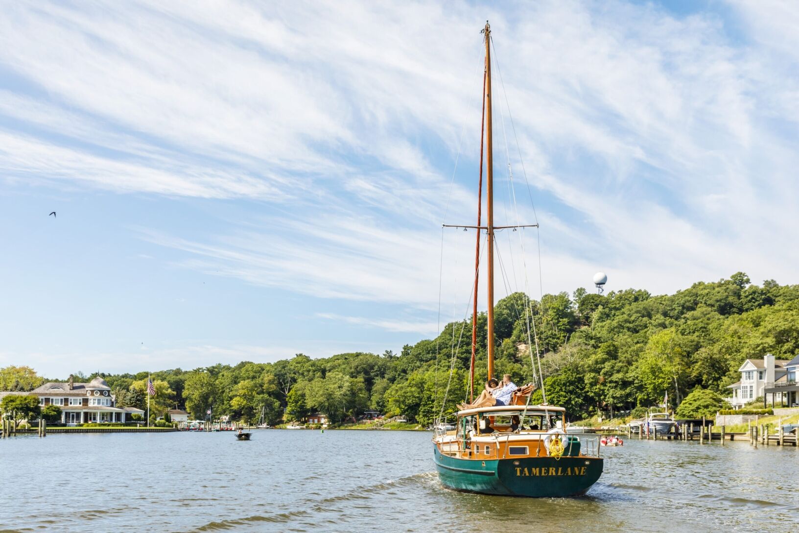 Two friends on top of a sail boat going down the channel. Lake houses and Mt. Baldhead are in the distance.