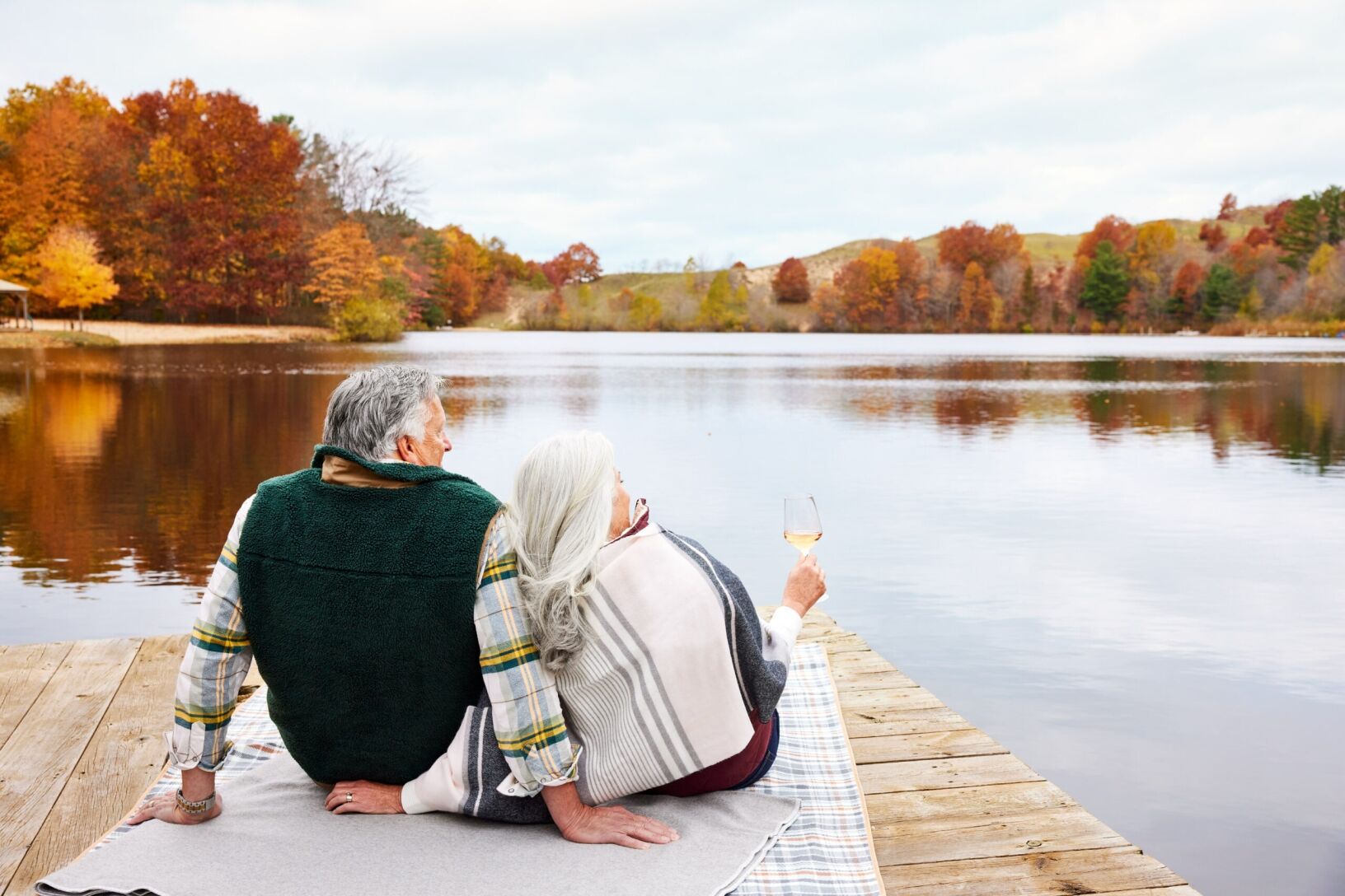 Couple sitting on a dock holding wine.