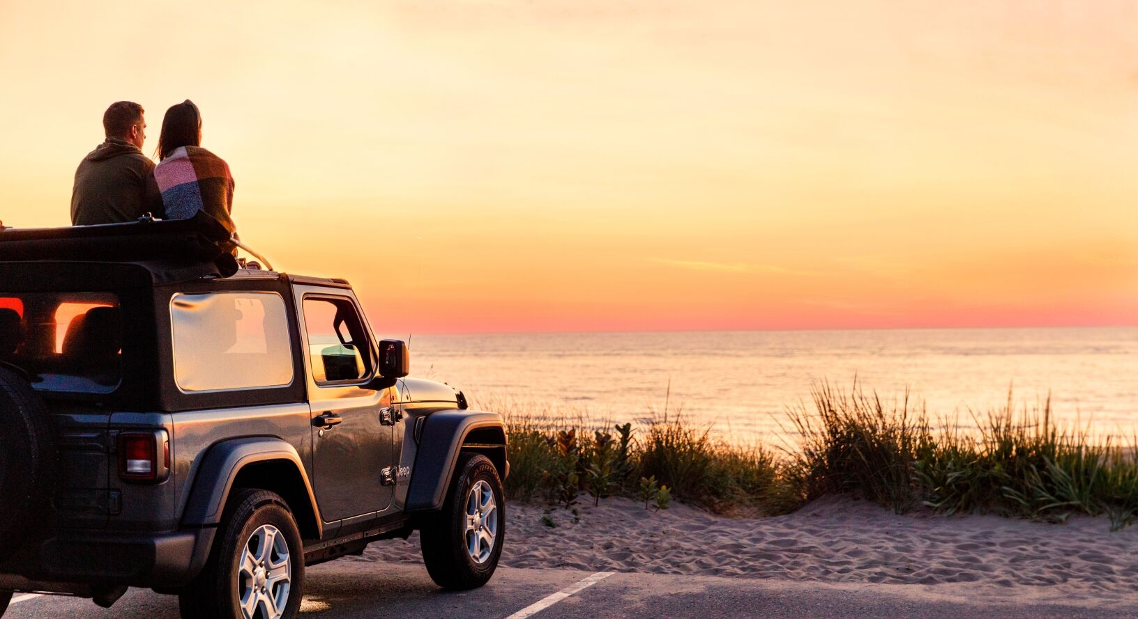 A couple watching the sunset from the top of their Jeep at Oval Beach.
