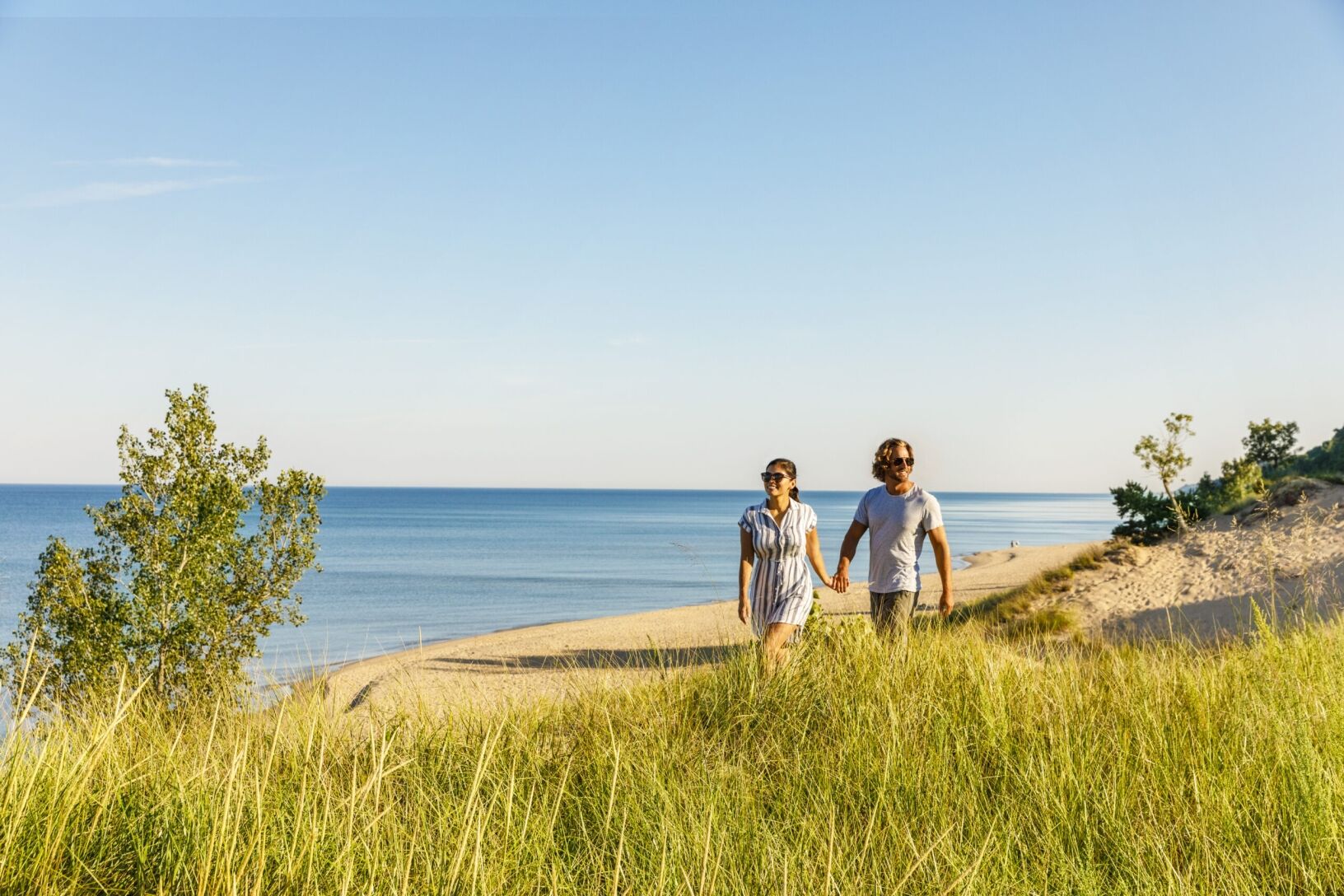 A couple with sunglasses holding hands as they hike the Saugatuck Dunes State Park.