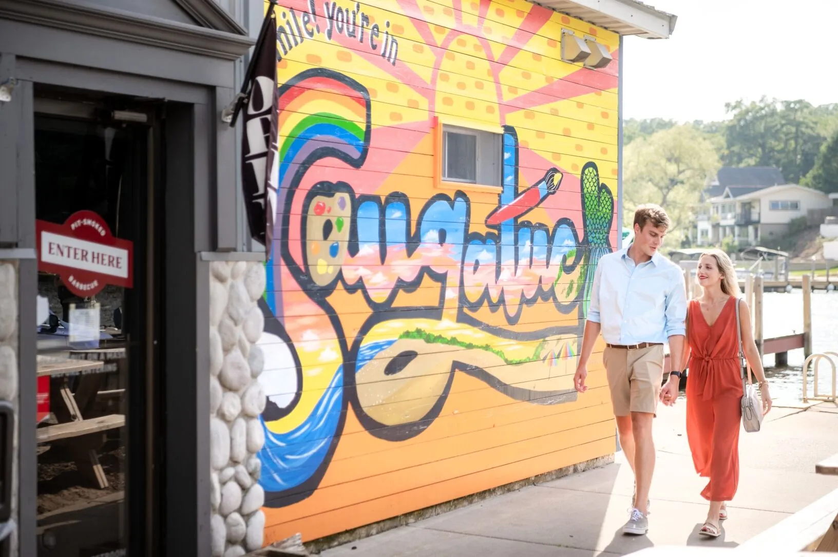 A couple walking past a mural near the water.
