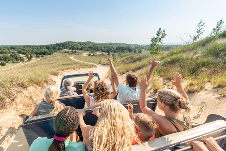 A group of people riding in a dune buggy with their hands in the air.
