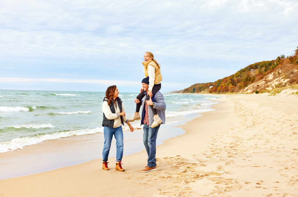 A couple and their daughter walking the shore of Saugatuck Dunes State Park in the fall.