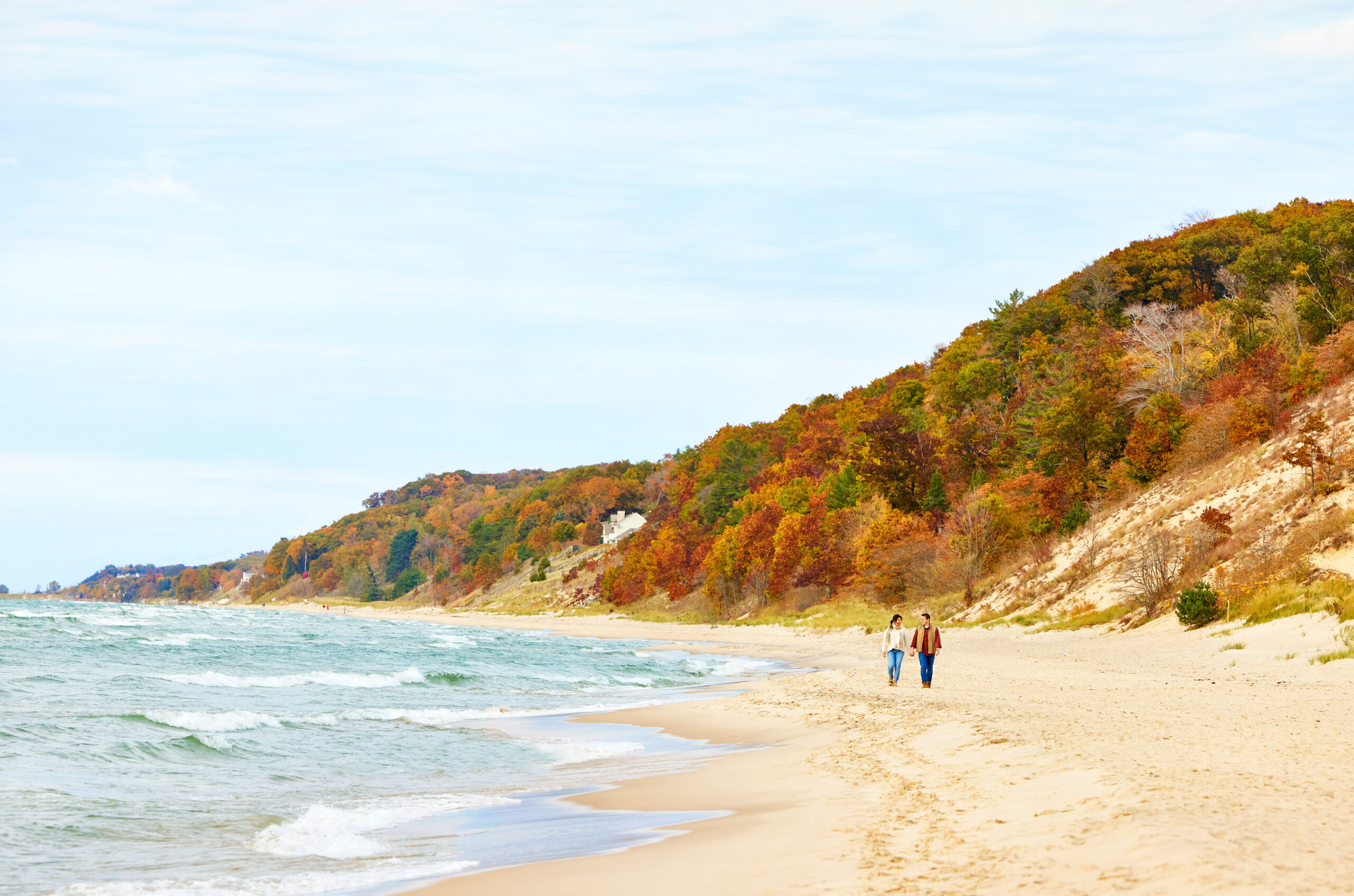 A couple walking the shore of Saugatuck Dunes State Park in the fall.