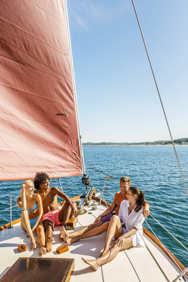 Four friends in swimsuits relaxing on top of a sail boat.