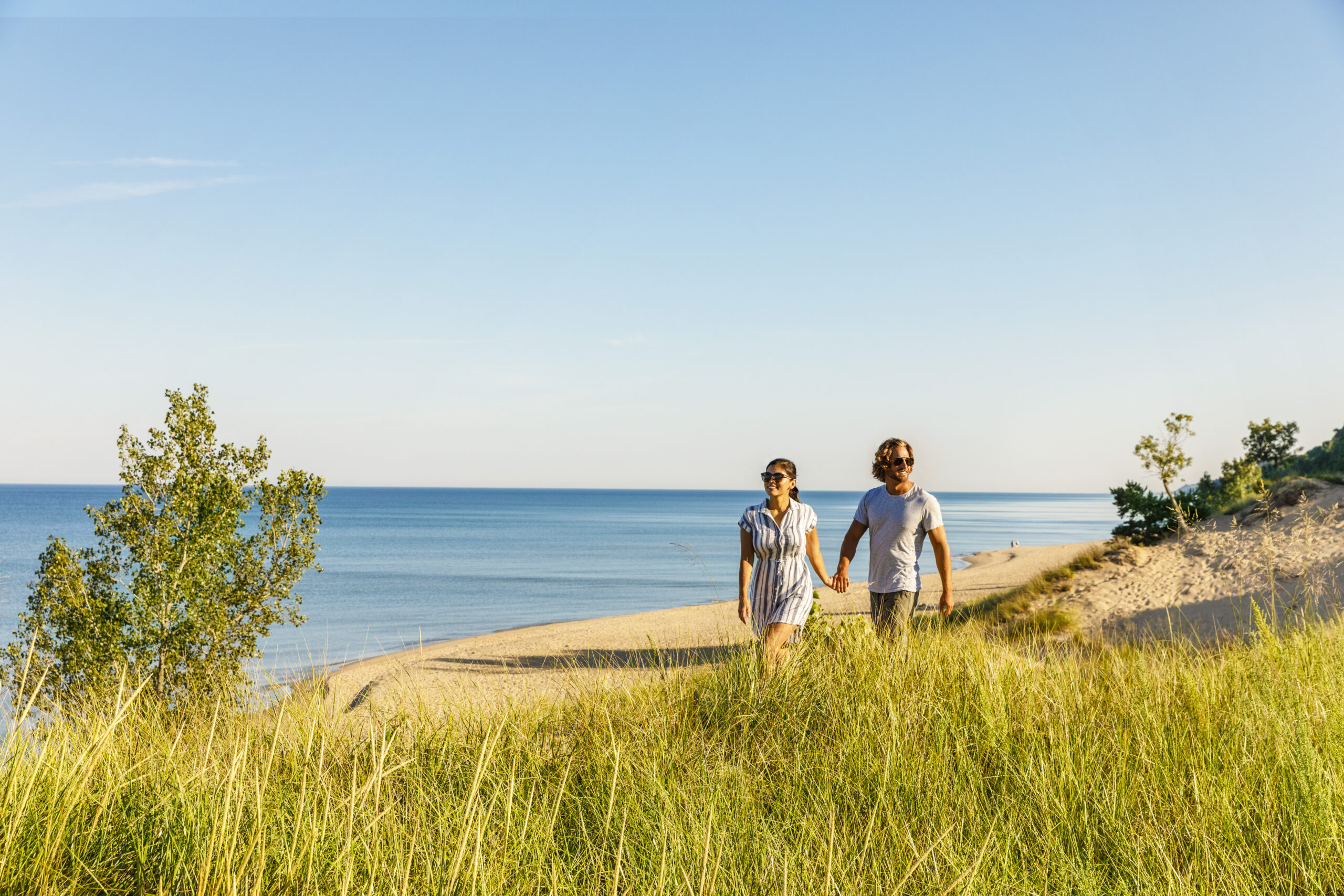 A couple with sunglasses holding hands as they hike the Saugatuck Dunes State Park.