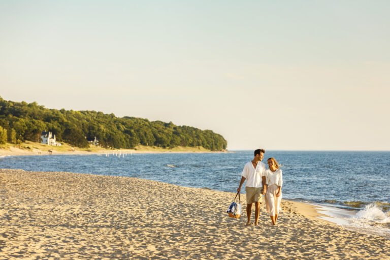 A couple holding hands and walking on the shore of Oval Beach.