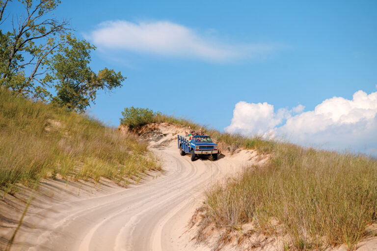 A group of people riding in a dune buggy with their hands in the air.