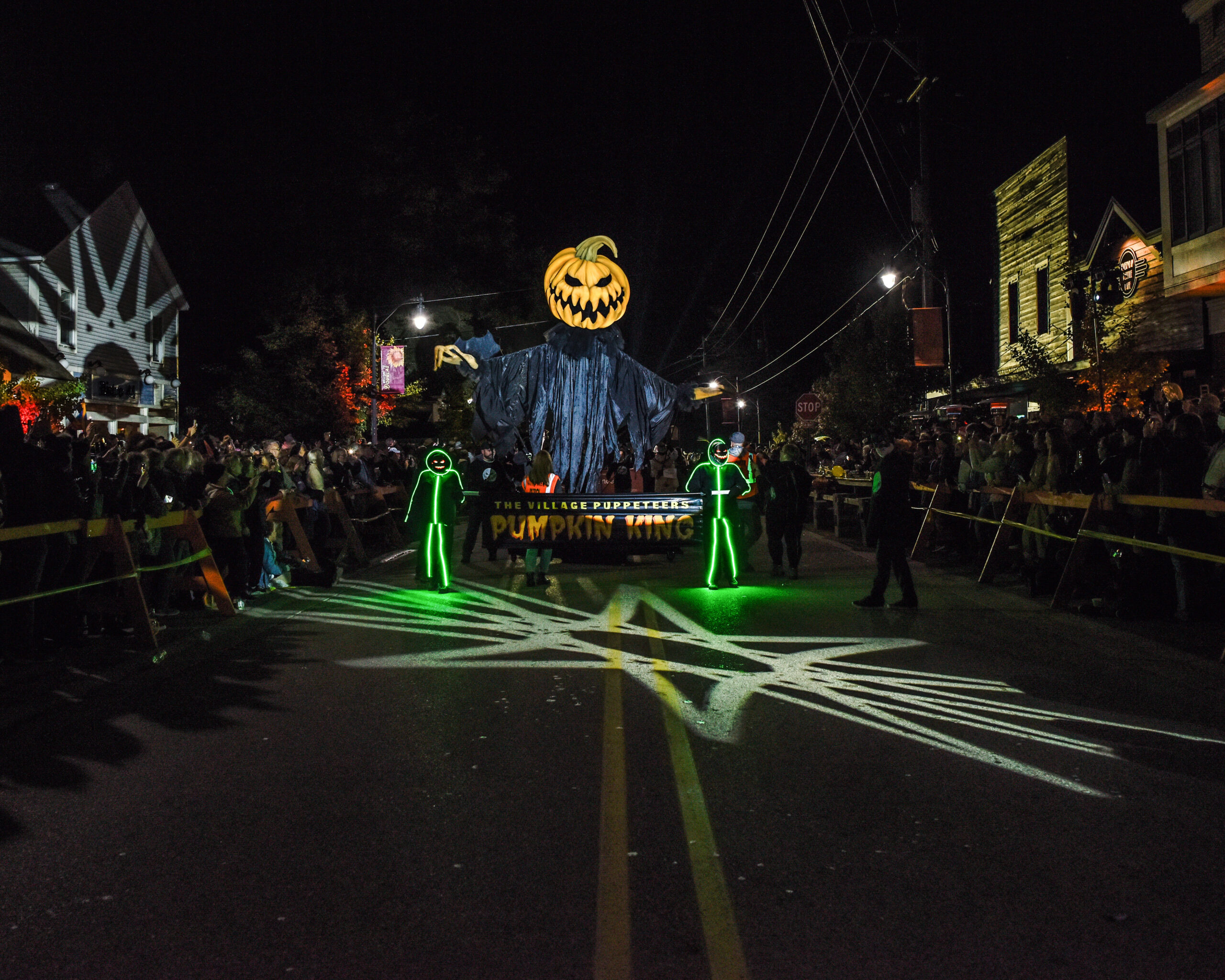 People in costumes line both sides of the street as a tall pumpkin parade float comes down the street for the Douglas Halloween Parade.
