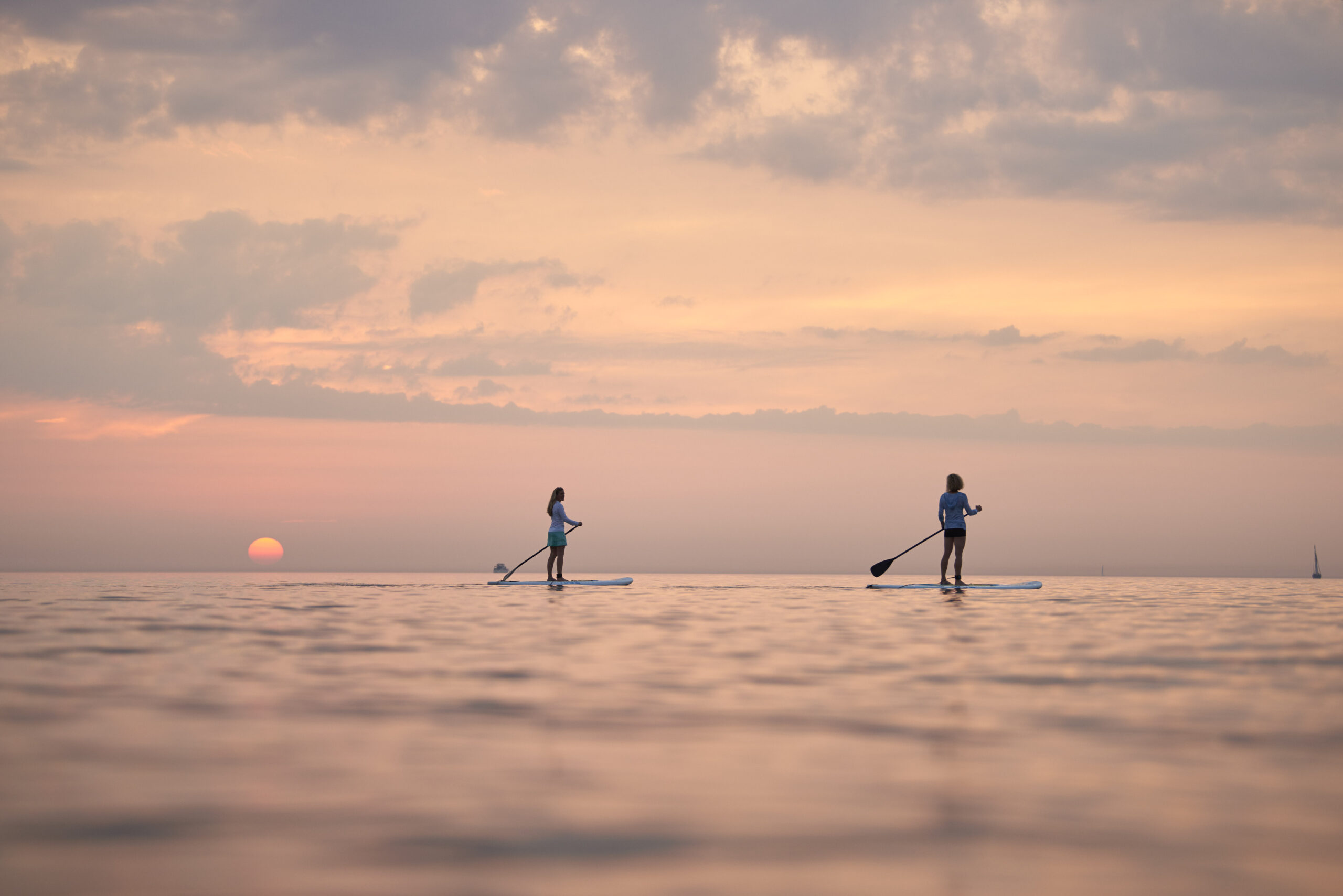 Two women standing on paddleboards as the sun sets over the lake.