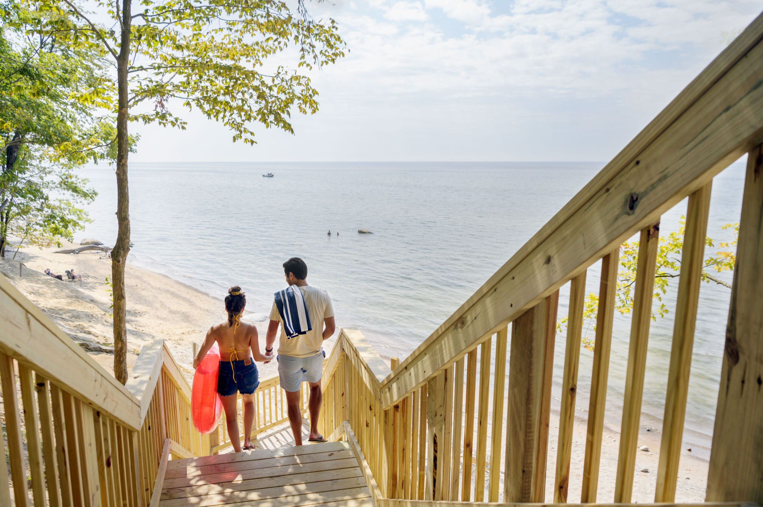 Man and woman walking down stairs to beach with beach gear.