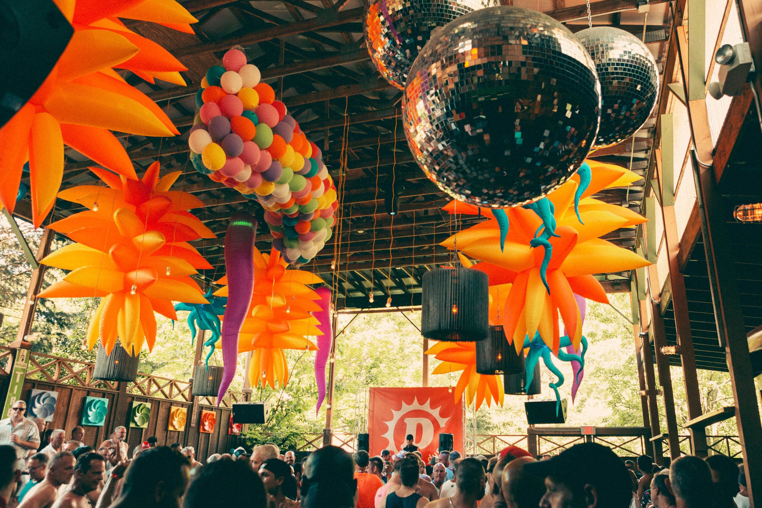 Crowd of people in a room with balloons and disco balls overhead