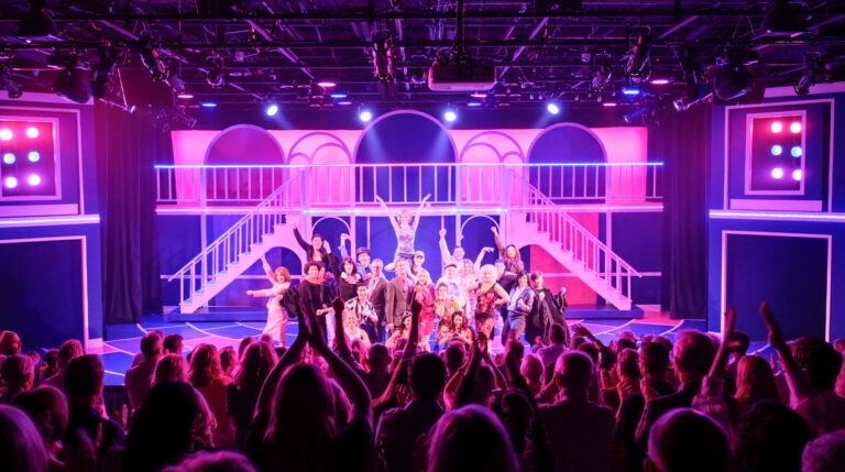 A large cast performing on stage at the Saugatuck Center for the Arts.