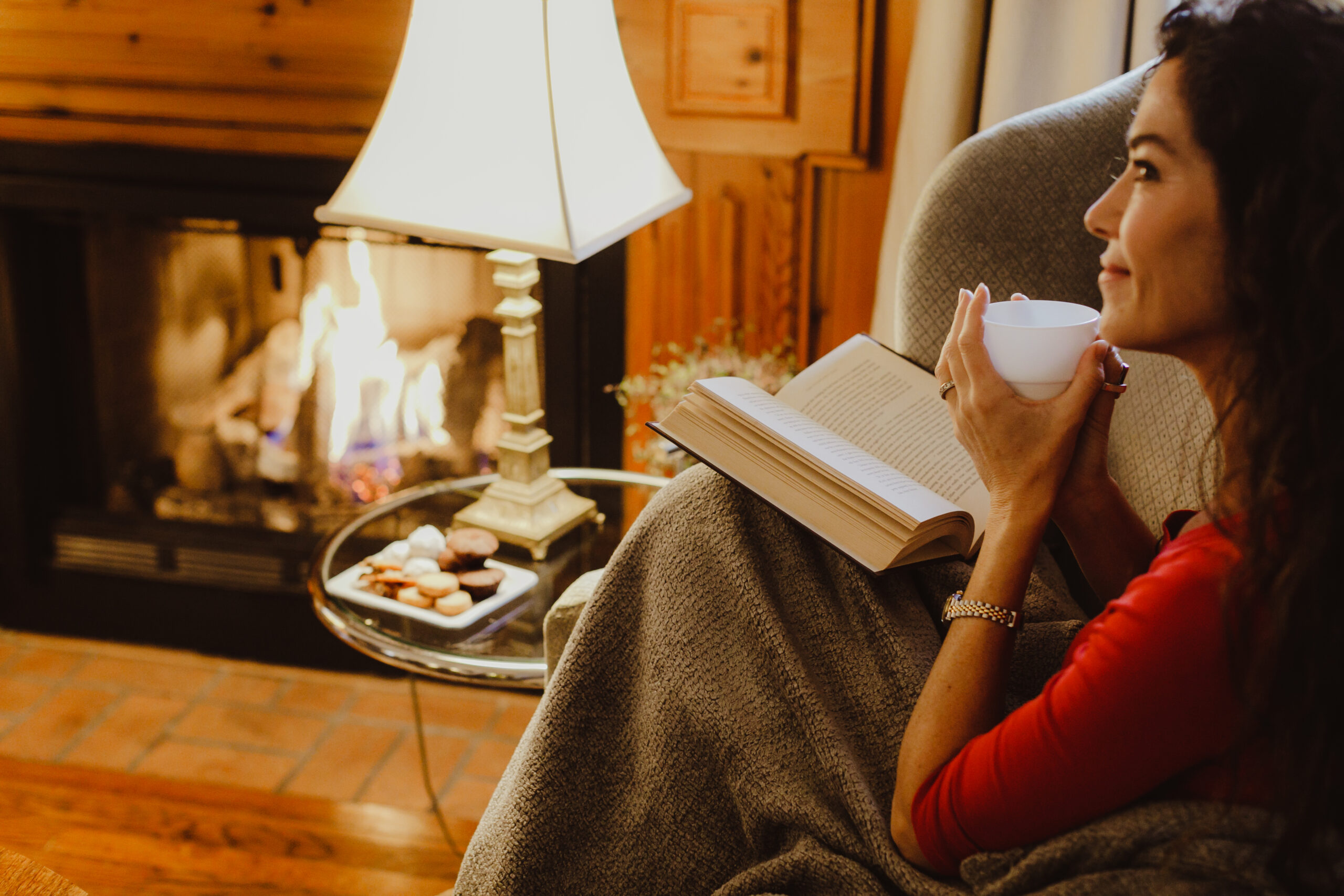Woman reading a book and sipping coffee by the fire